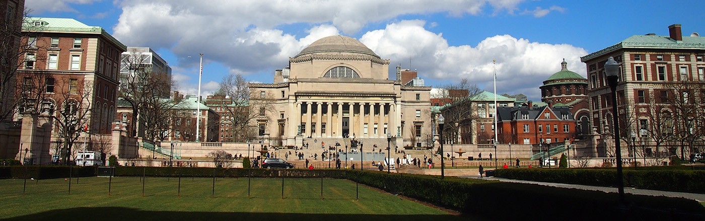Low Memorial Library, with its grand steps and granite dome, sits at the center of Columbia's Morningside campus, as large cumulus clouds float across a bright, blue sky