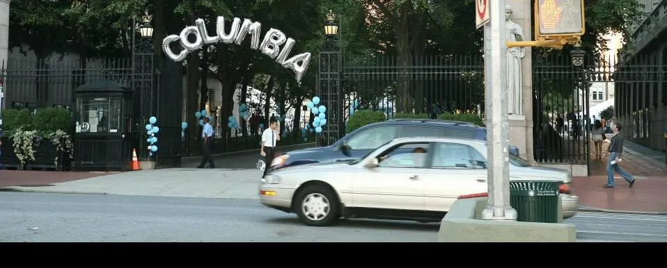 Intersection of 116th and Broadway with cars zooming past and Columbia balloons on the gates